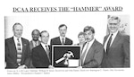 black and white photo of 7 individuals in business suits holding an award