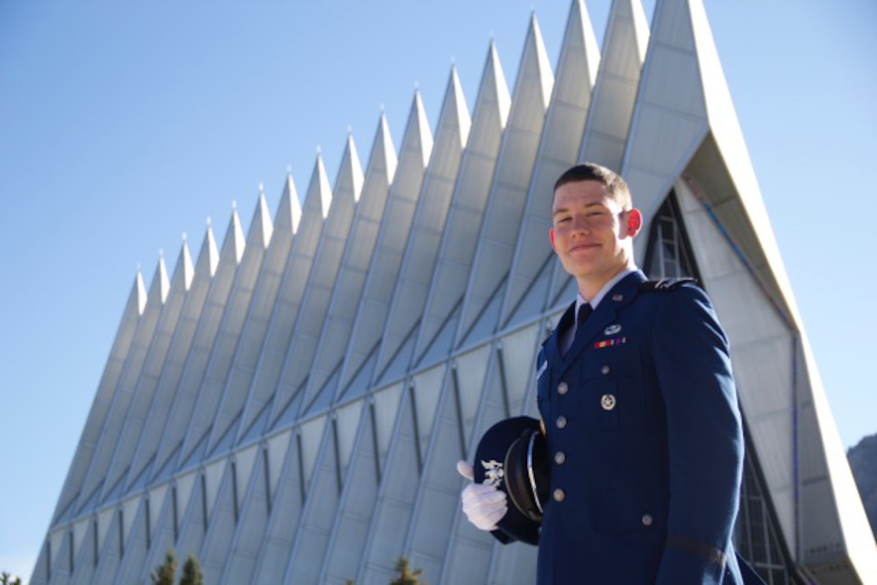 An Air Force Academy cadet smiles in front a modern chapel
