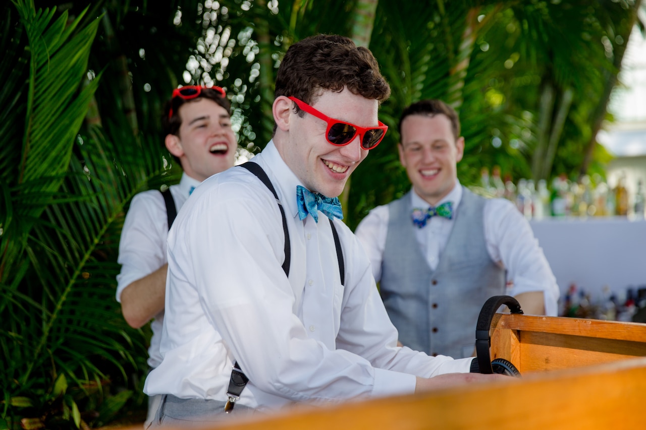 A man in sunglasses smiles while DJing an an outdoor celebration.
