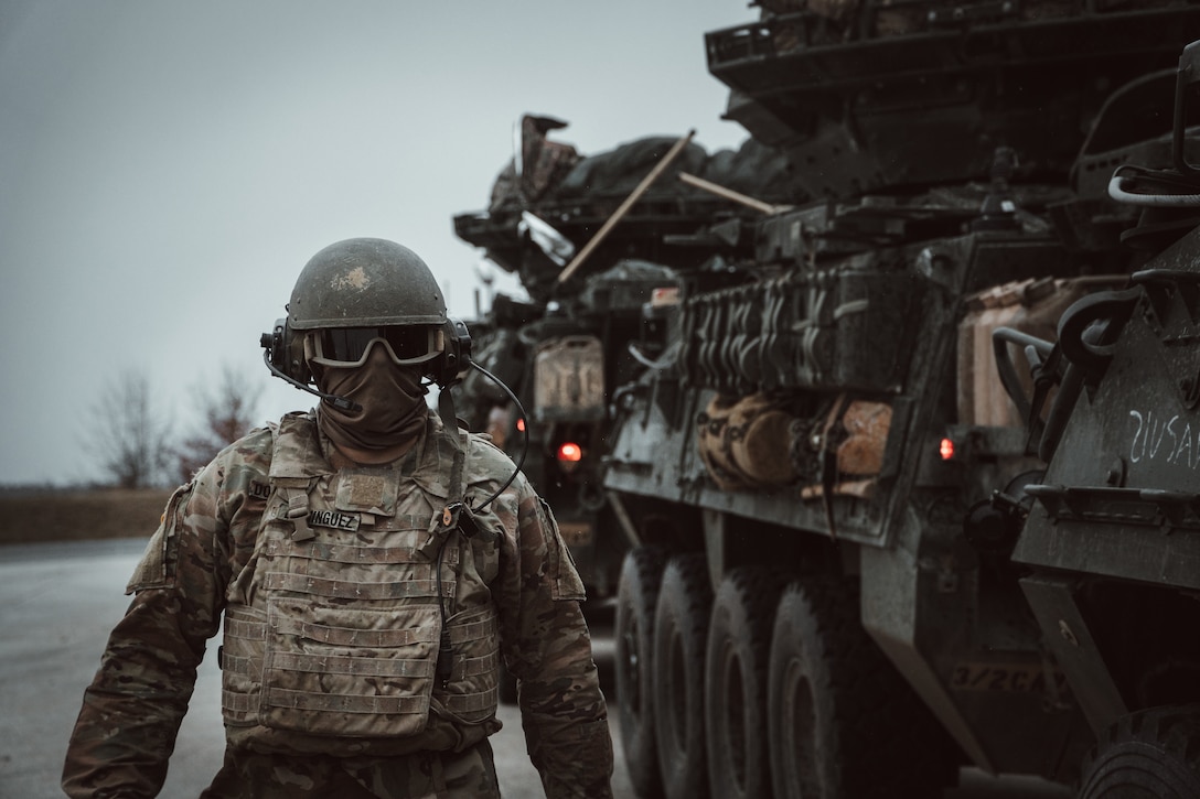 A soldier walks next to a large military vehicle.