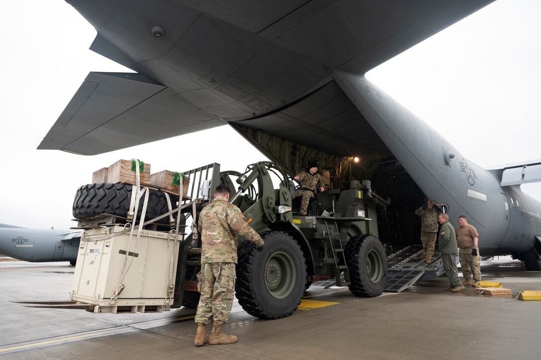 Large containers of supplies are loaded into the back of a military aircraft.