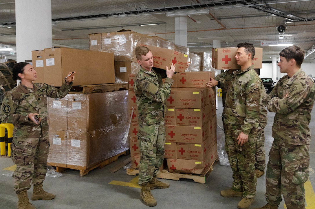 Soldiers unload boxes of supplies from pallets in a storage room.