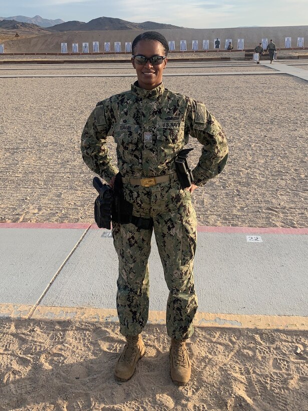 A woman in military fatigues stands in a desert area.