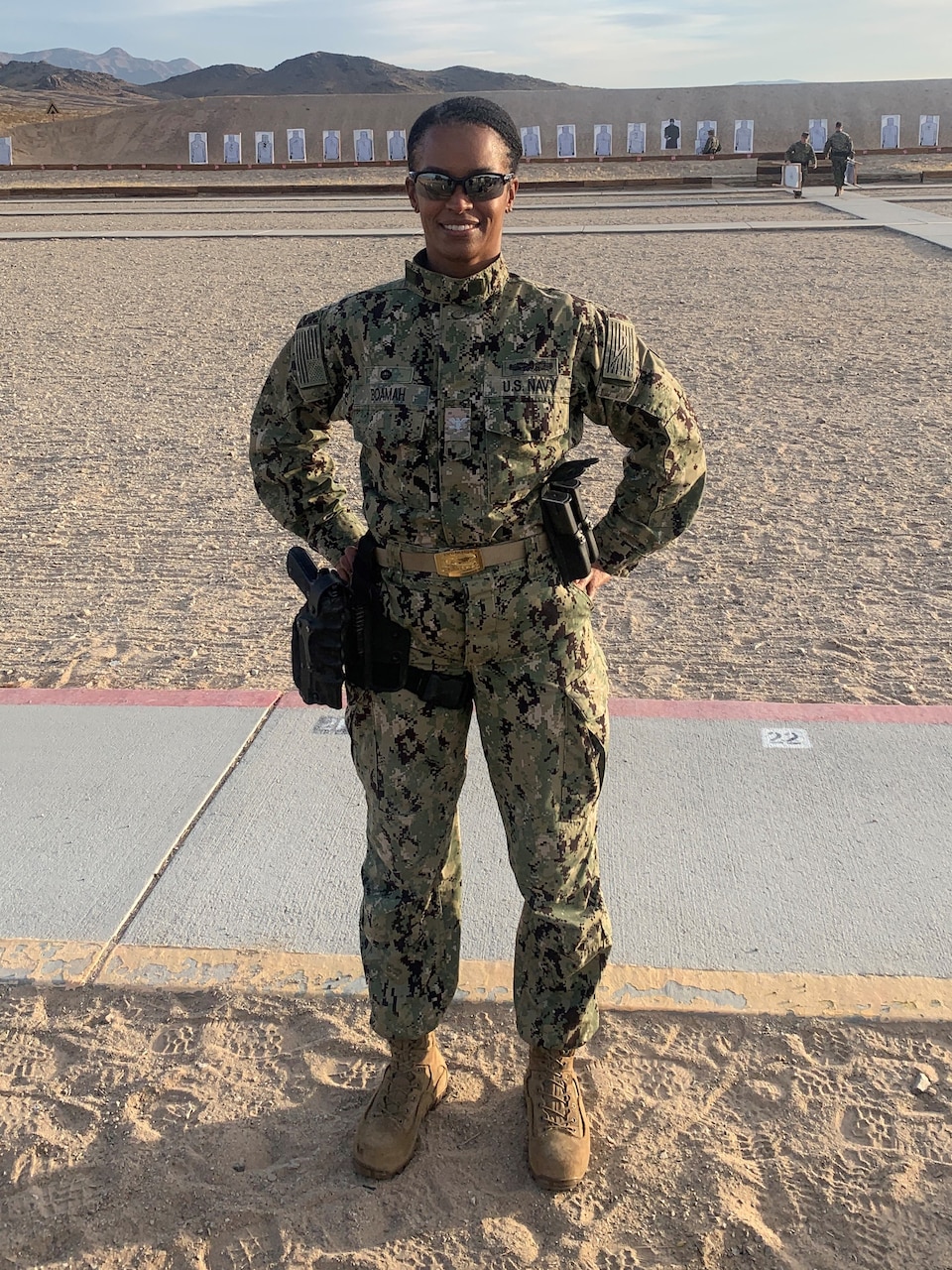 A woman in military fatigues stands in a desert area.