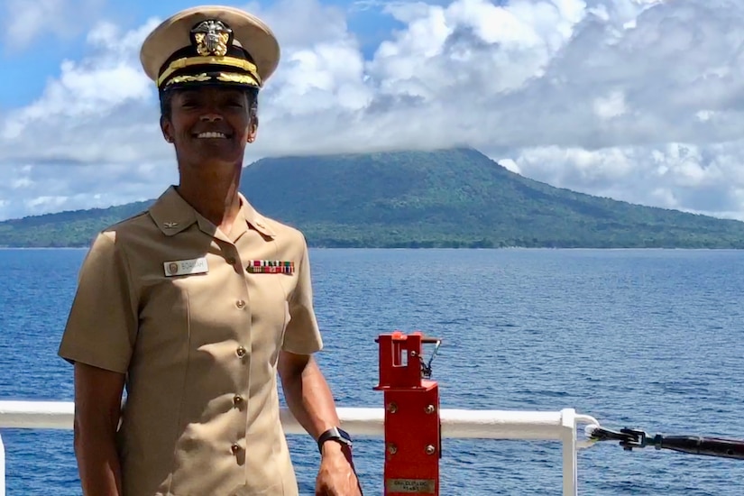 A woman in uniform stands on the deck of a ship overlooking an island.