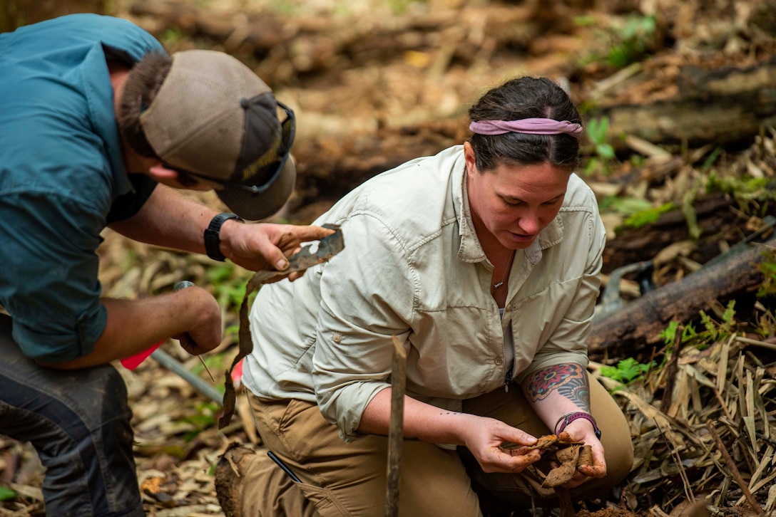 Two people look through materials in the woods.