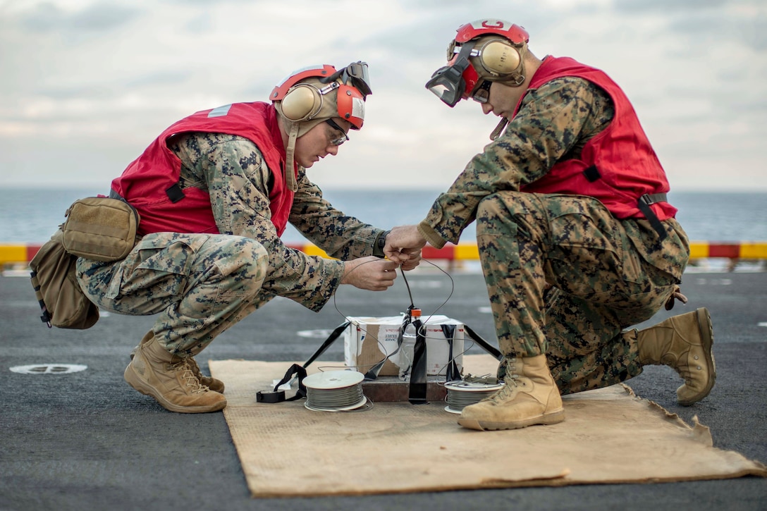 Two Marines work on an explosive device during training aboard a ship at sea.