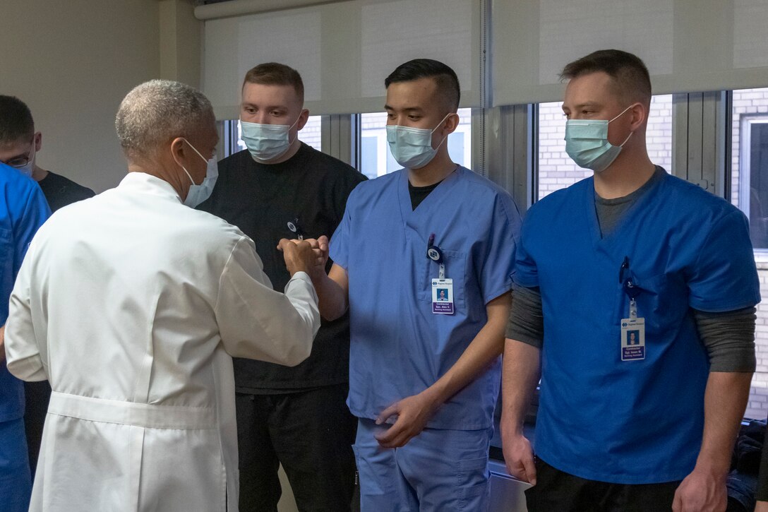 A group of people in medical uniforms stand in a row while another man gives them a fist bump.