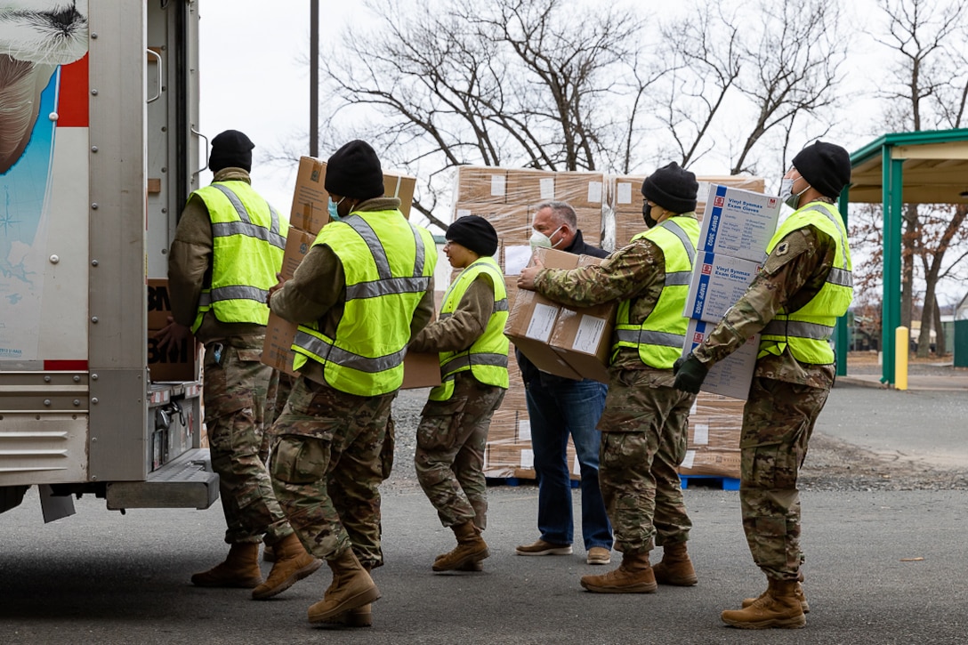 A group of soldiers carries boxes to the back of a truck.