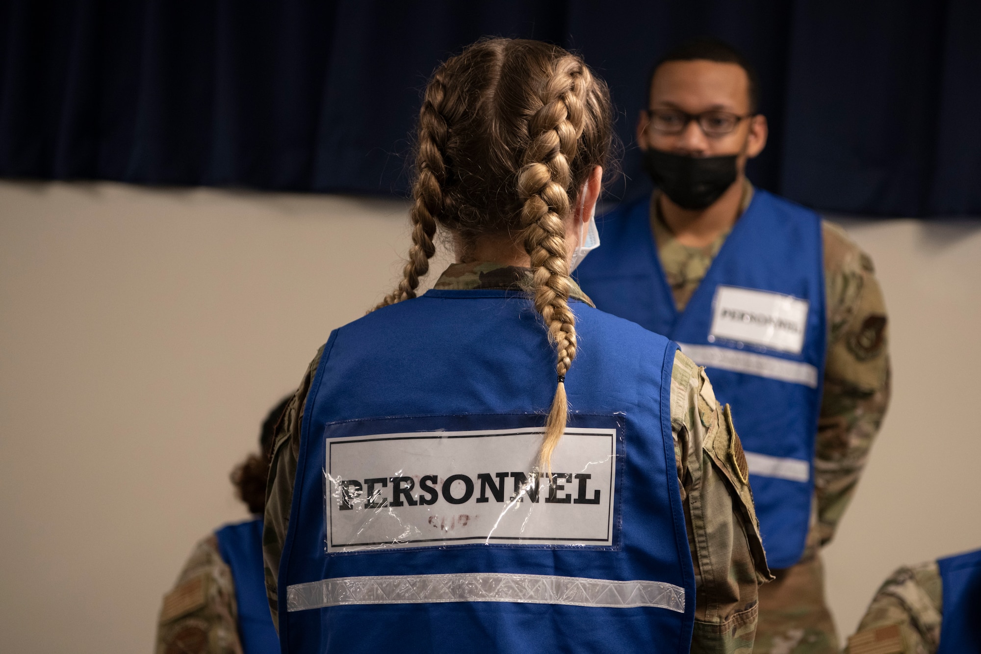 2 Airmen with blue vests wait to guide personnel through a line