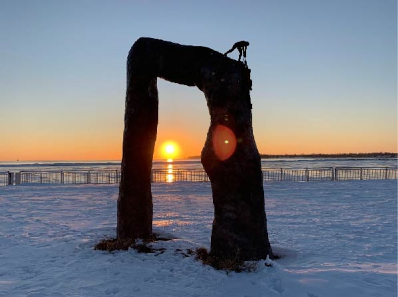 Arch sculpture standing in snow with sunset in background.