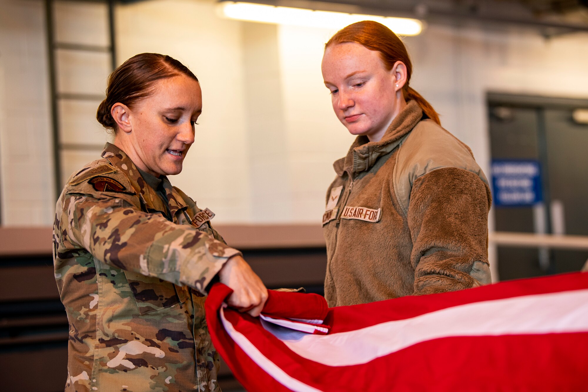 U.S. Air Force Staff Sgt. Haley Bradshaw, left, 423rd Air Base Group honor guard NCO in charge, provides instruction on flag folding to Airman 1st Class Alyssa Richmond, 423rd Communications Squadron cyber surety apprentice, RAF Alconbury, England, Feb. 9, 2022. Airmen from the 423rd ABG honor guard conduct weekly training sessions to hone their skills and build chemistry in executing details with Airmen from different squadrons. (U.S. Air Force photo by Senior Airman Eugene Oliver)