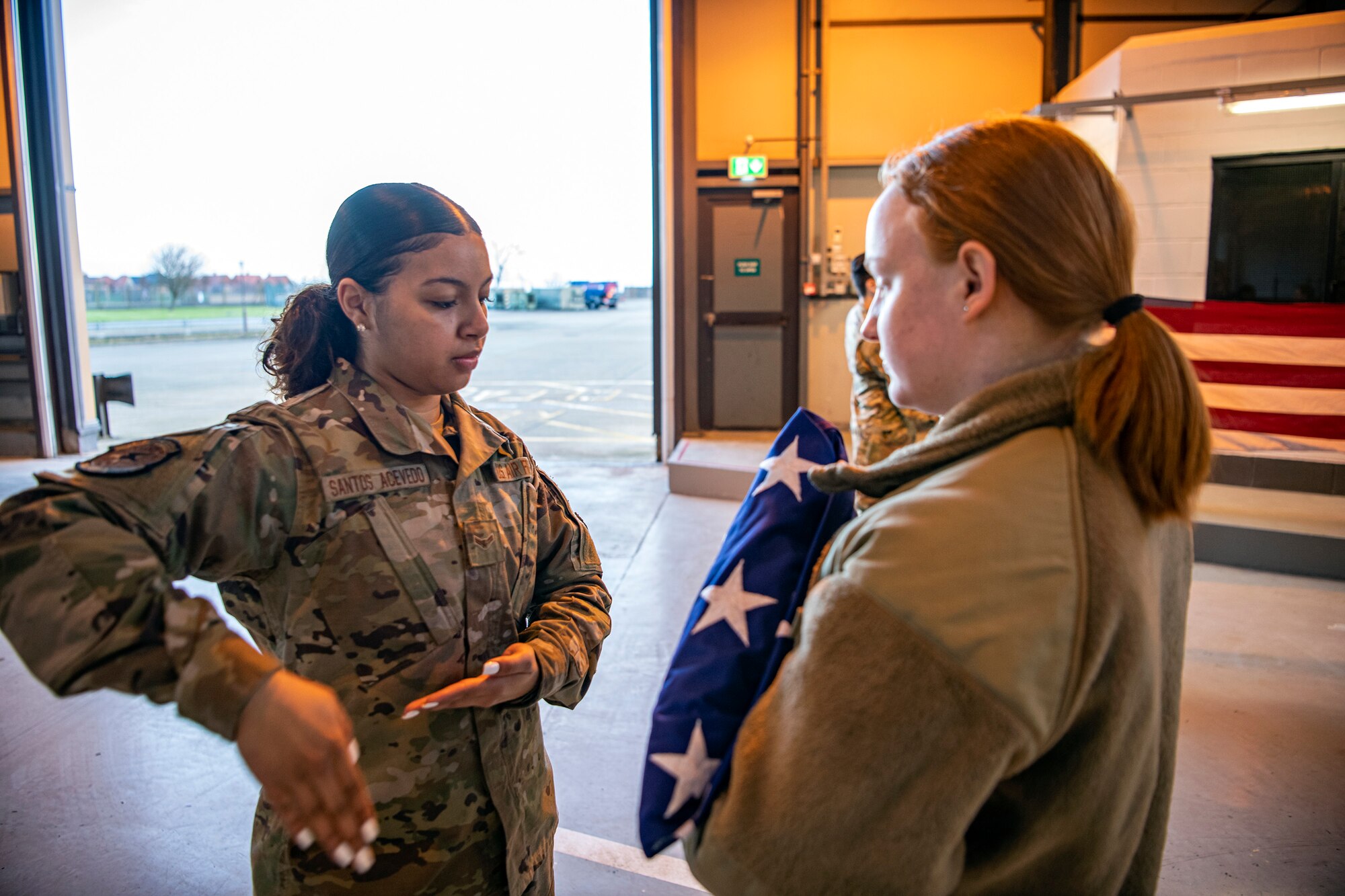 Airman 1st Class Jenesi Santos Acevedo, U.S. Air Forces in Europe and Air Forces Africa Air Postal Squadron, Detachment Five mail processing specialist, gives instruction on how to dress a flag at RAF Alconbury, England, Feb. 9, 2022. Airmen from the 423 Air Base Group honor guard conduct weekly training sessions to hone their skills and build chemistry in executing details with Airmen from different squadrons. (U.S. Air Force photo by Senior Airman Eugene Oliver)