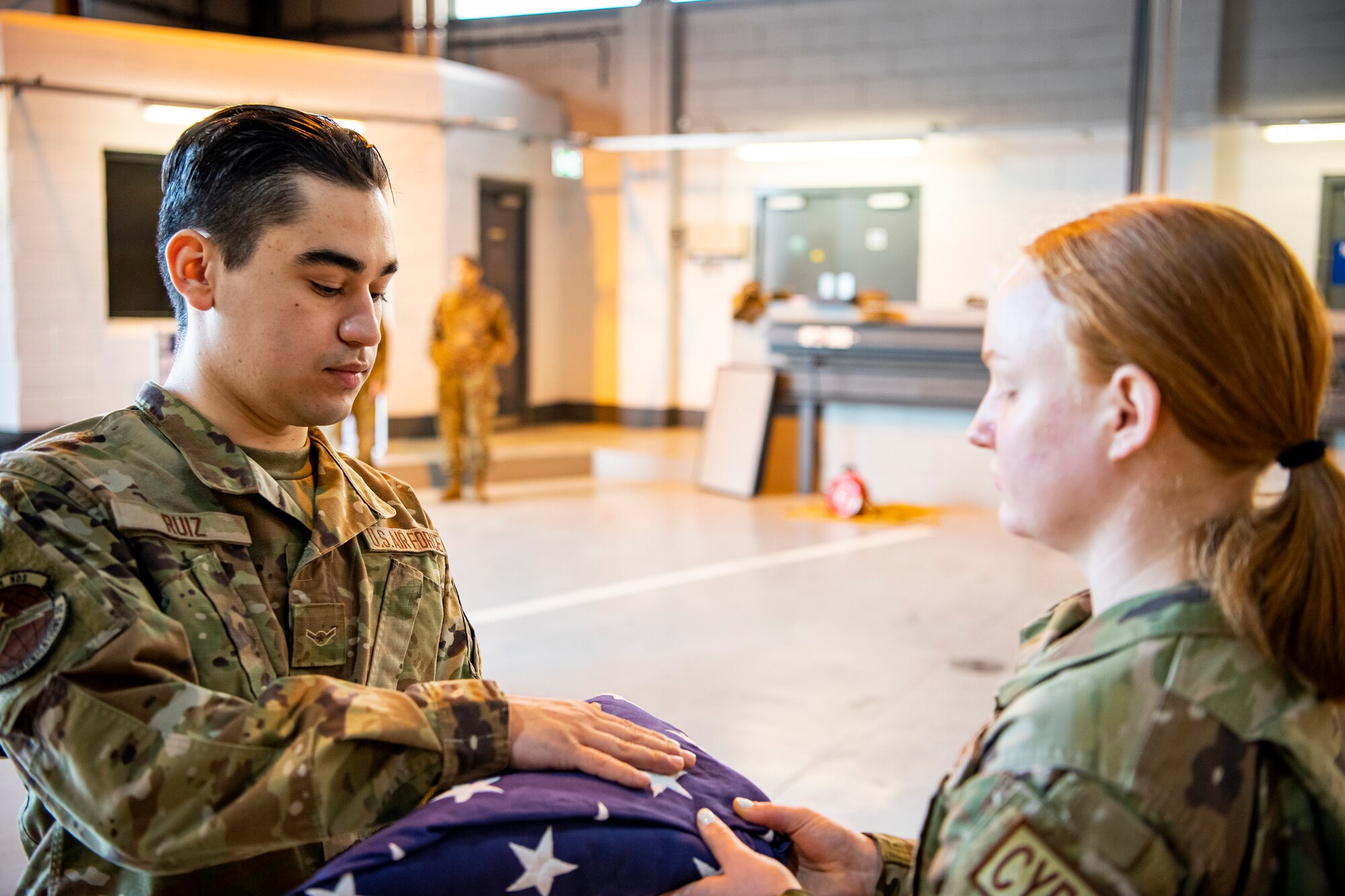 U.S. Air Force Airman Francisco Ruiz, left, 423rd Communications Squadron client systems apprentice, hands a folded flag to Airman 1st Class Alyssa Richmond, 423rd Communications Squadron cyber surety apprentice at RAF Alconbury, England, Feb. 9, 2022. Airmen from the 423 Air Base Group honor guard conduct weekly training sessions to hone their skills and build chemistry in executing details with Airmen from different squadrons. (U.S. Air Force photo by Senior Airman Eugene Oliver)