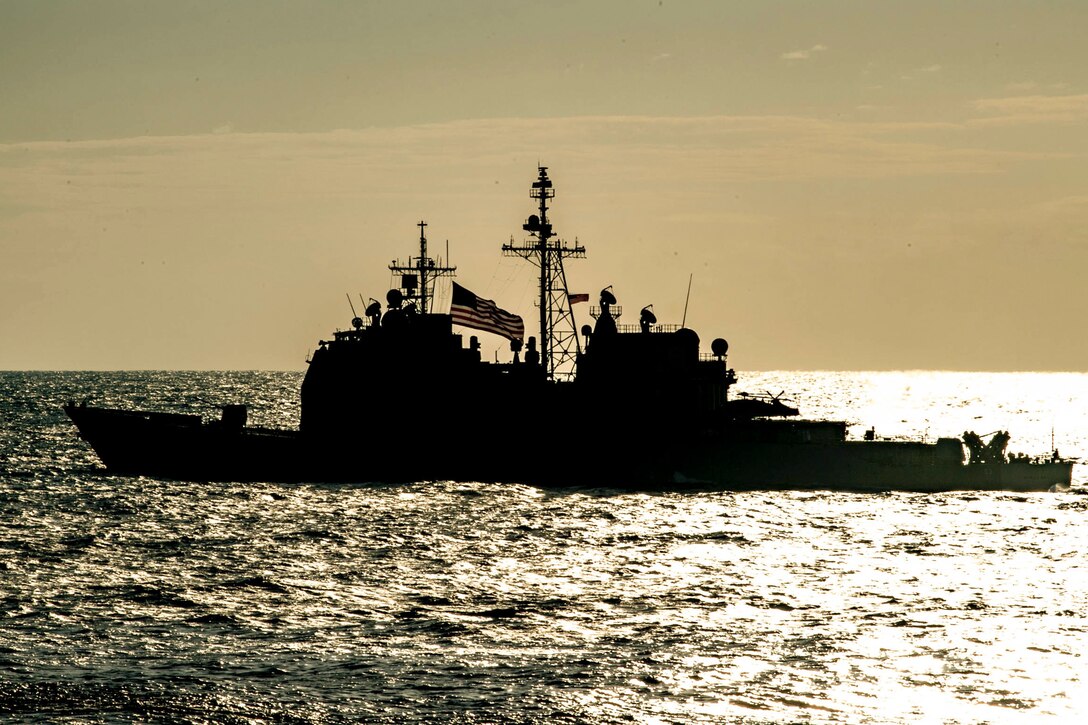 A ship sails in a body of water as shown in silhouette.