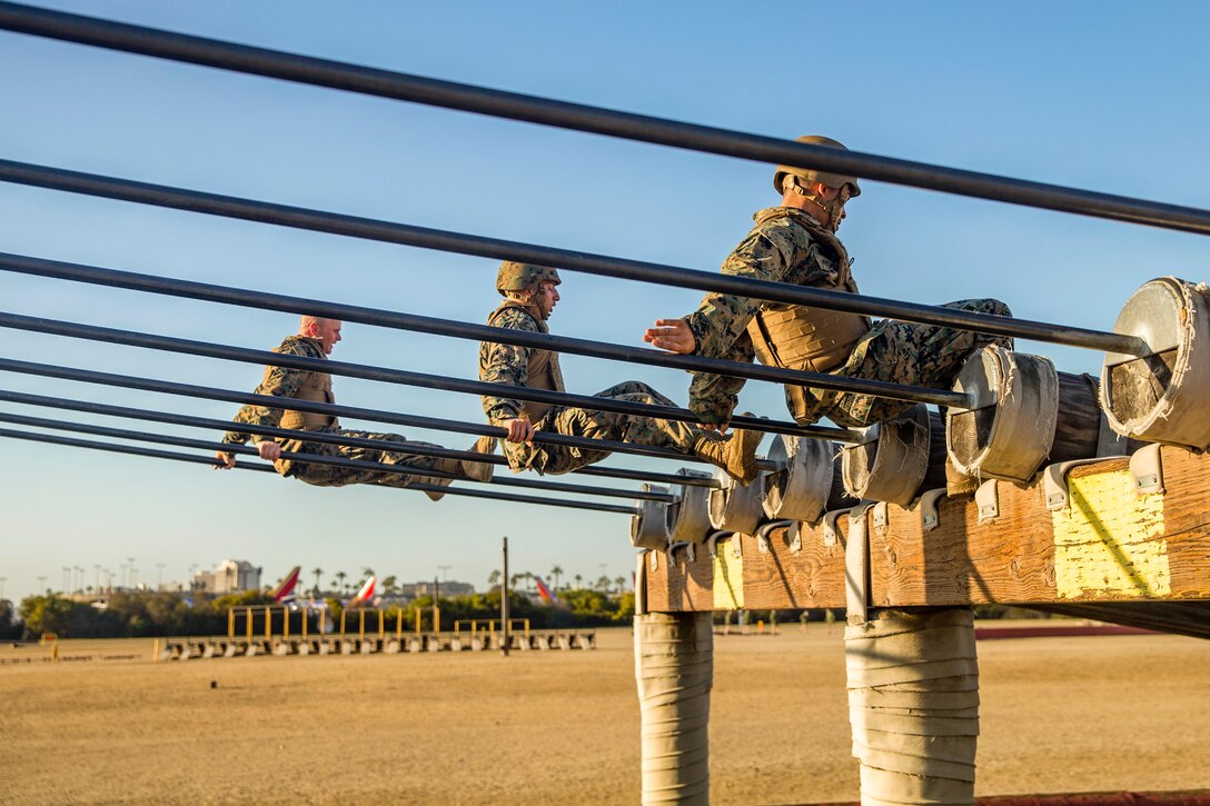 Three Marines maneuver across a jungle gym.