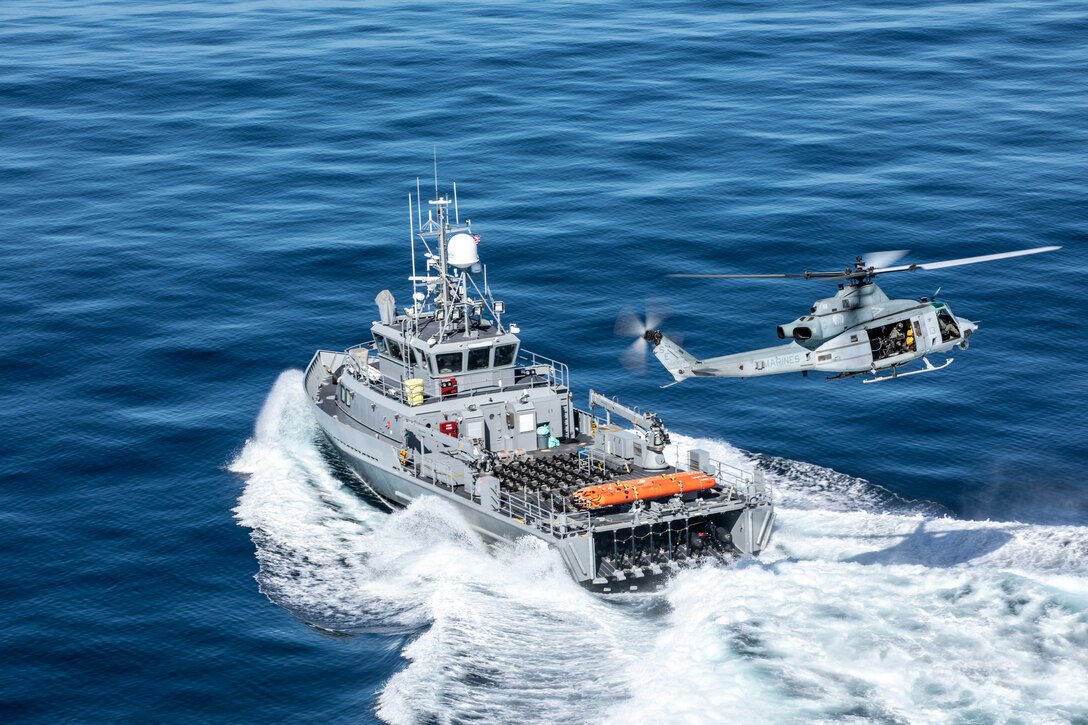 A helicopter flies above a boat in the ocean.