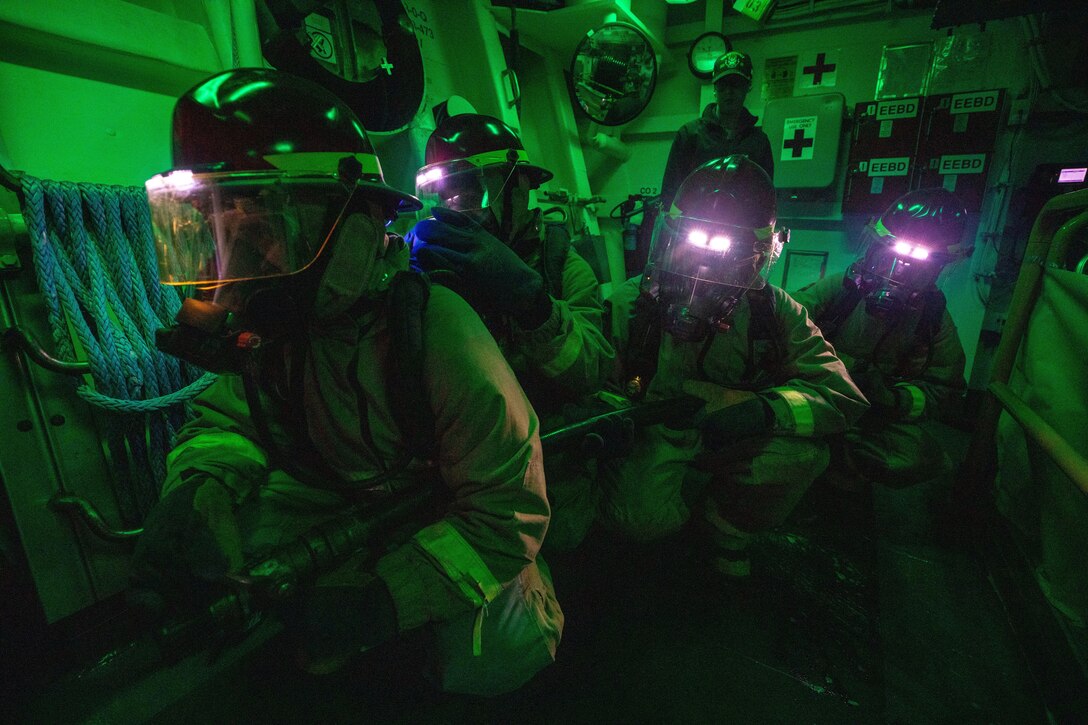 Sailors hold a hose in a dark room.