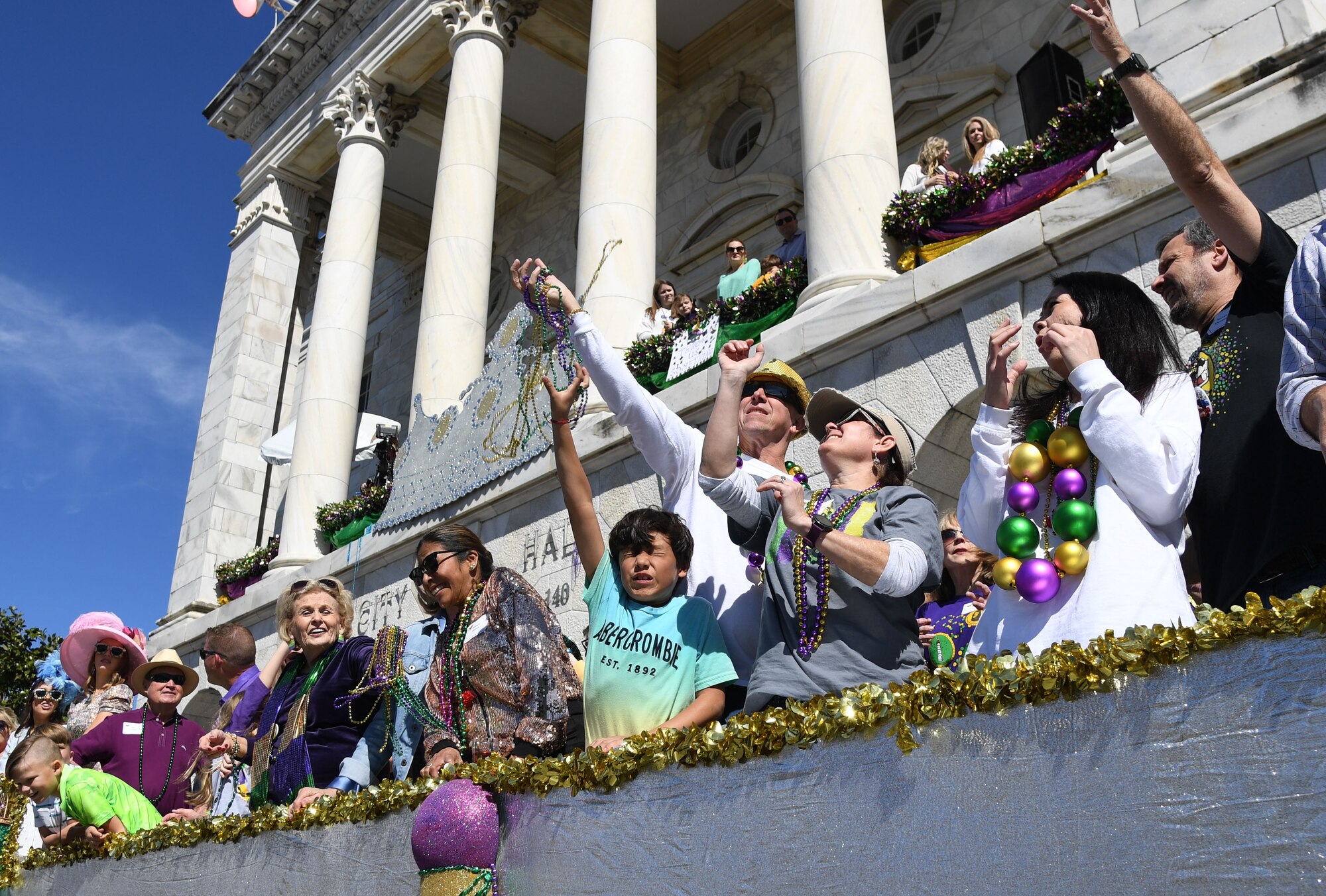 Leadership from Keesler Air Force Base reaches for bead necklaces tossed to them from floats during the Gulf Coast Carnival Association Mardi Gras parade in Biloxi, Mississippi, March 1, 2022. Keesler personnel participate in local parades every Mardi Gras season to show their support of the communities surrounding the installation. (U.S. Air Force photo by Kemberly Groue)