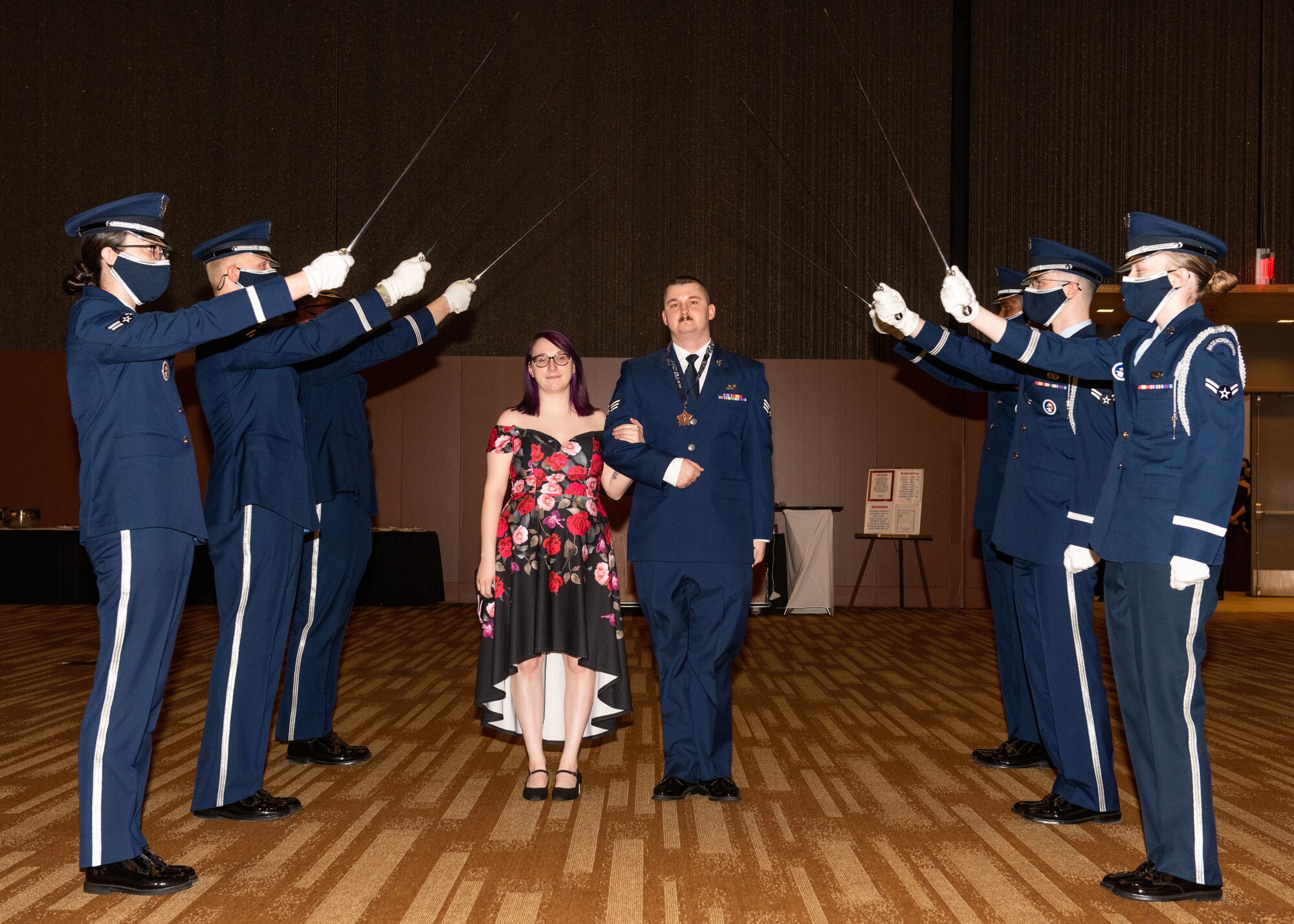 An award nominee and his wife walk under an arch of sabers.