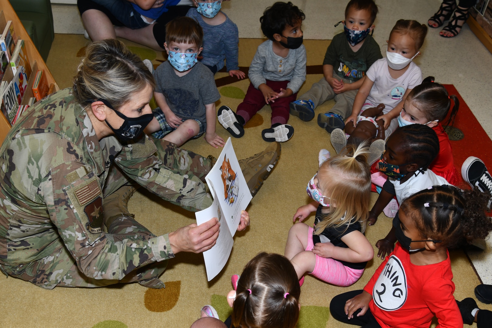 A woman in military uniform reads a book to children.