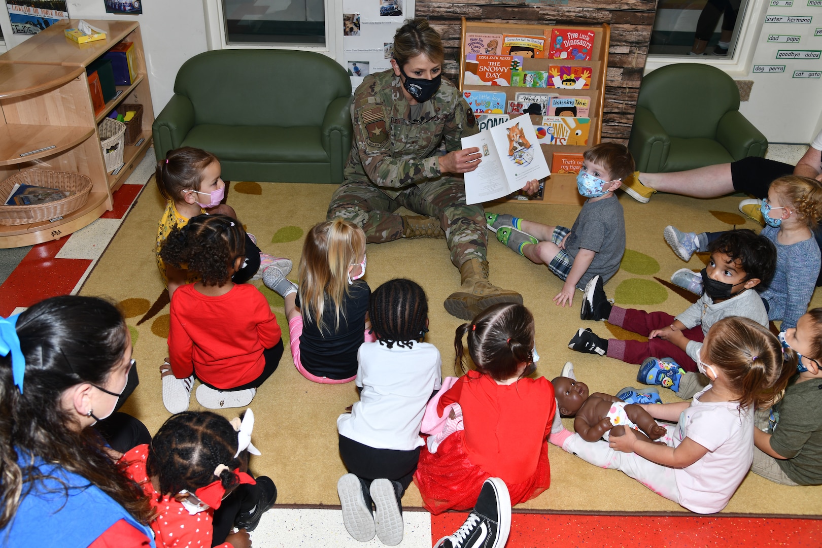 Woman in military uniform reads a book to children.