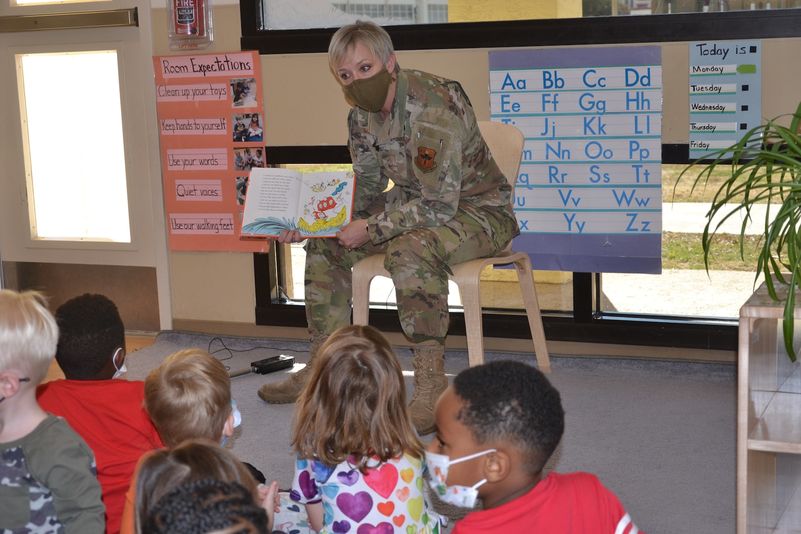 Woman in military uniform reads a book to small children.