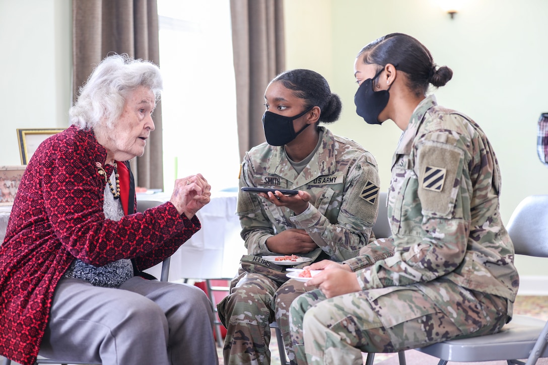 Two soldiers speak to an older woman.