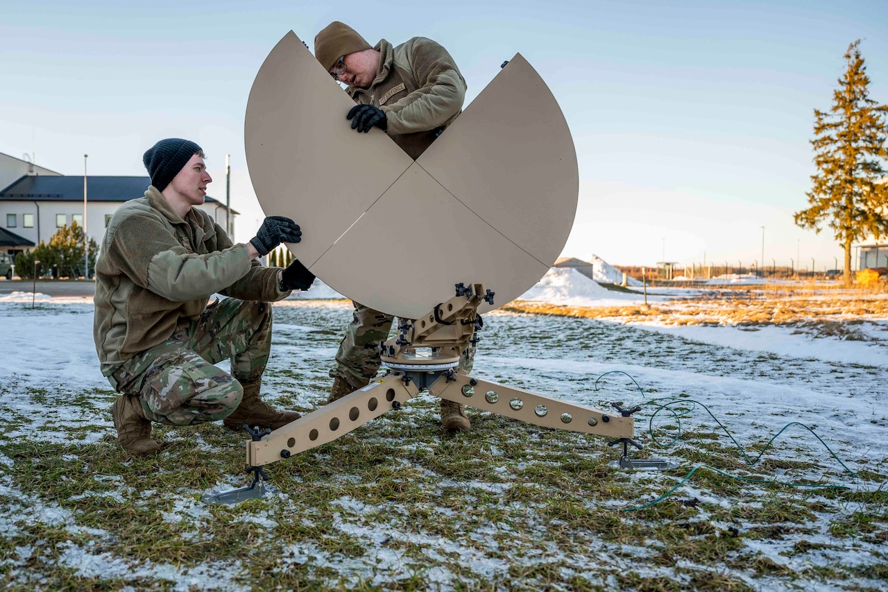 Two service members work on a satellite dish.