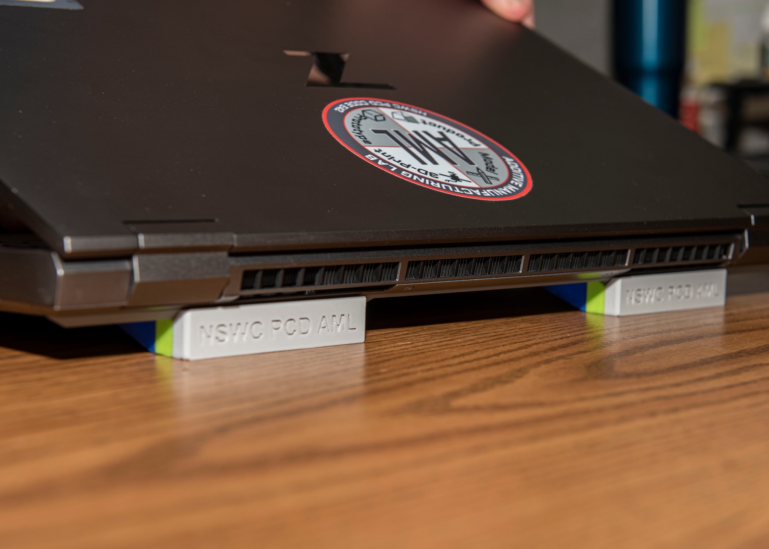 An installed Laptop Lifter (aka the Tide Riser). Naval Surface Warfare Center Panama City Division's Codes E15 Hydrospace Laboratory and E42 Additive Manufacturing Lab (AML) collaborated to produce this solution to help improve ventilation to the division's new computers to keep them from overheating due to prolonged use. The innovation is installed at the rear of the computer to improve air flow. The final product is estimated to cost $2 per unit which offers a significant savings versus $6 - $8 per unit if it were produced externally. (U.S. Navy photo by Eddie Green)