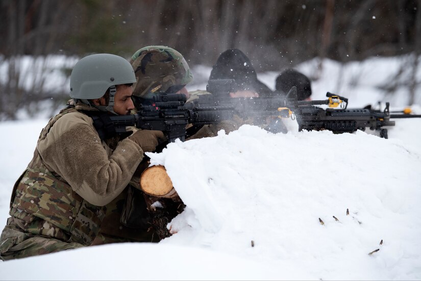 Airmen and Guardsmen take cover behind an arctic defensive fighting position.