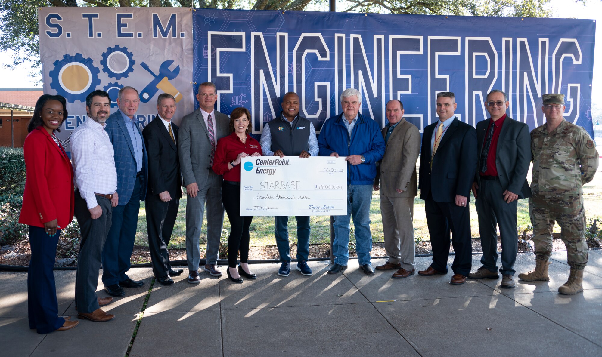 Twelve adults stand in from of an engineering sign holding a large check for $14,000.