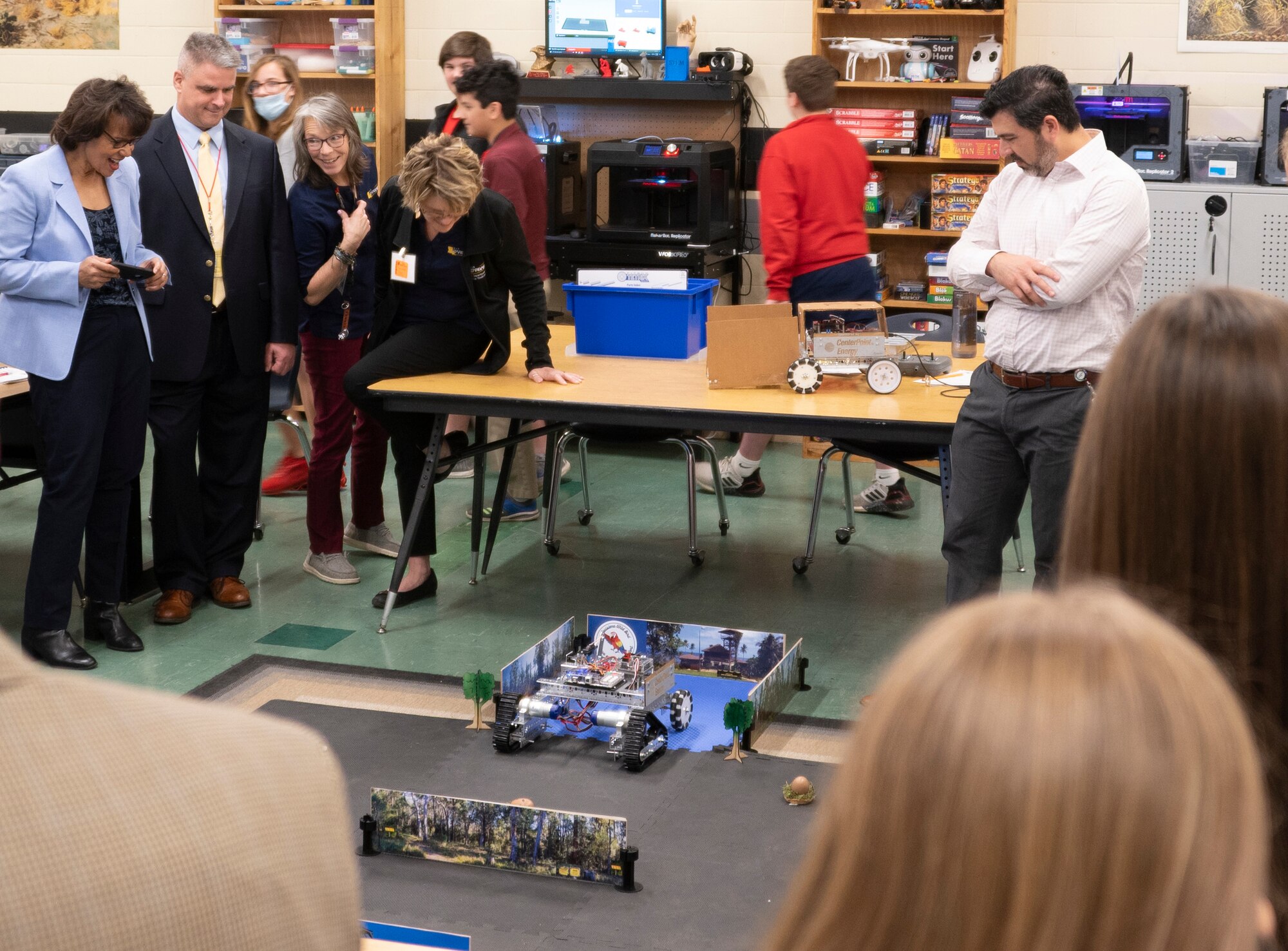 Men and women stand around a robot moving on the ground.