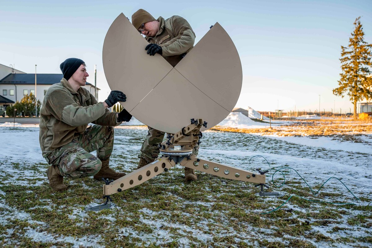 Two service members work on a satellite dish.