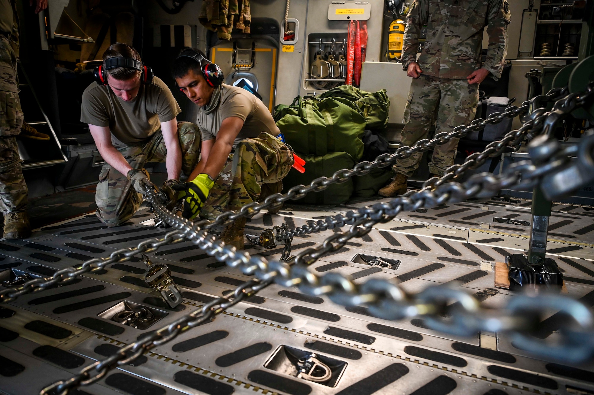 U.S. Air Force Senior Airman Nicholas Smail (left) and Senior Airman  Christopher Geer, both assigned to the 732nd Air Mobility Squadron, Joint Base Elmendorf-Richardson, Alaska, chain down equipment onto a C-17 Globemaster III during Operation Talon Lightning on Andersen Air Force Base, Guam, March 4, 2022.