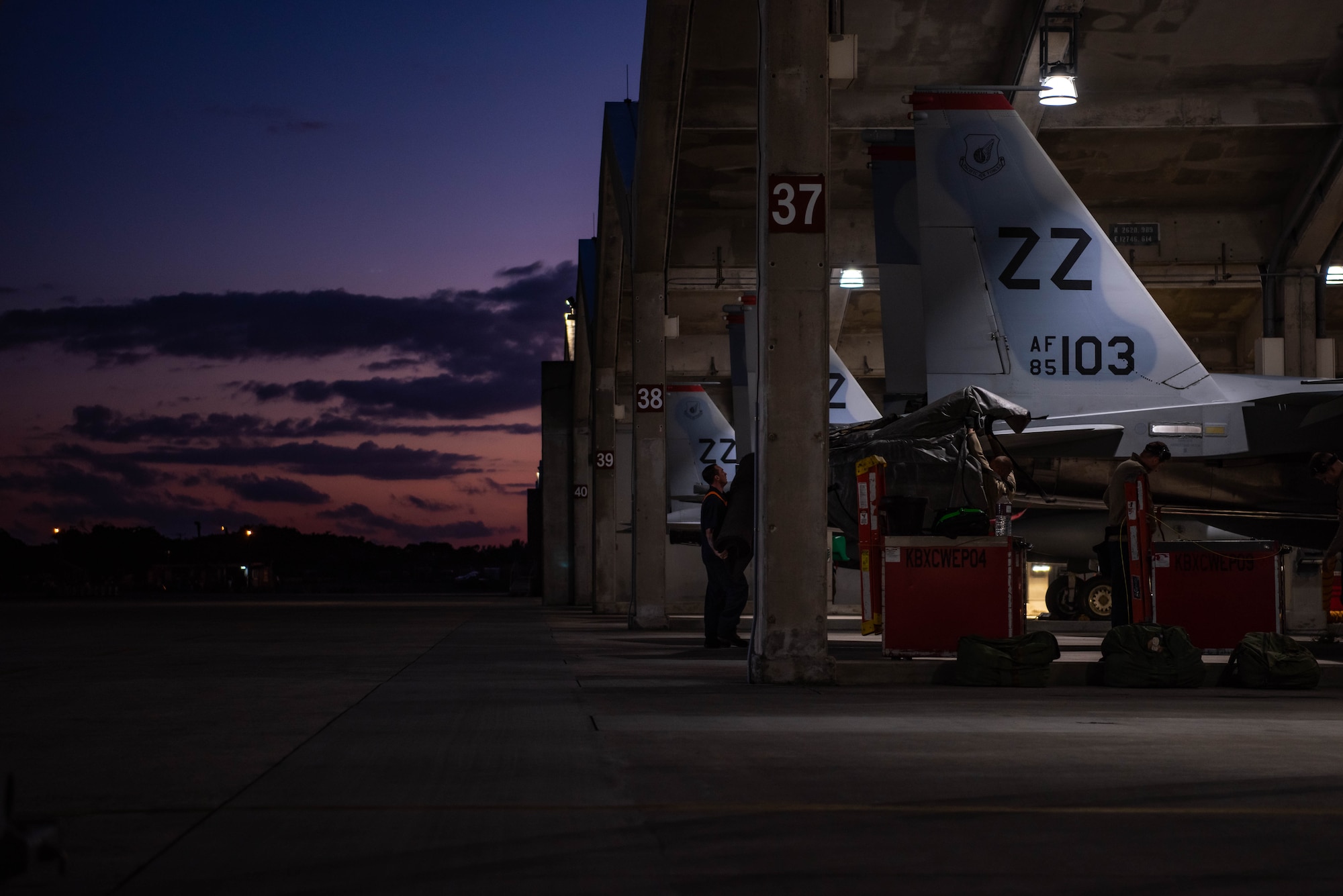 Airmen download munitions from a F-15C Eagle at dusk.