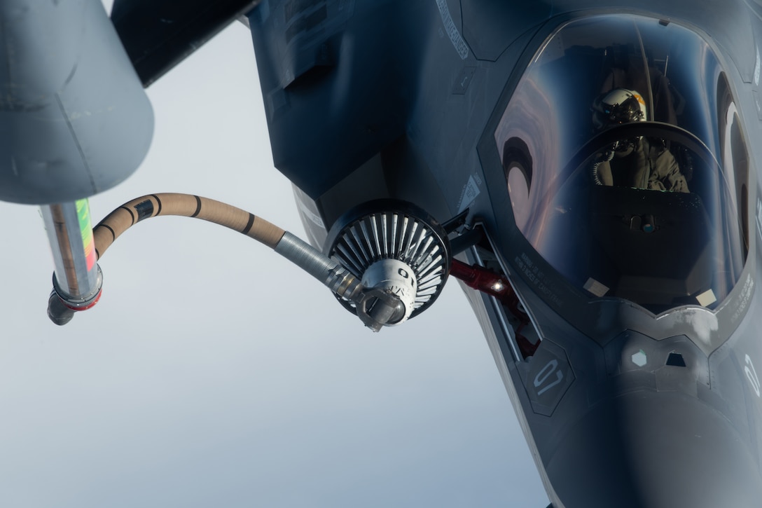 A military jet is refueled in midair using a hose attached to another aircraft.