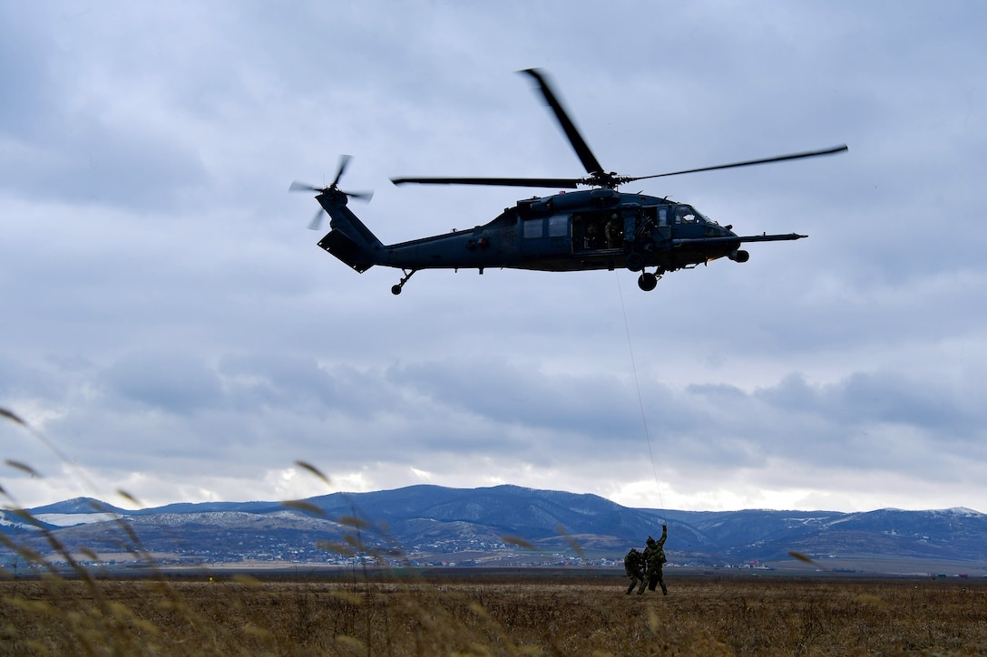 Service members prepare to hoist into a helicopter.