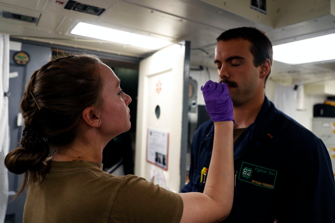 A sailor wearing gloves administers a COVID-19 test to another sailor.