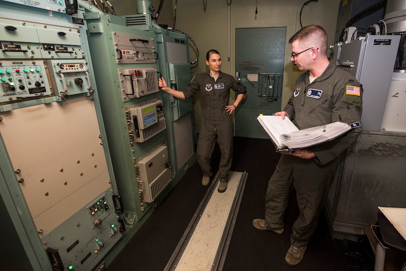 Two airmen stand beside large network devices.