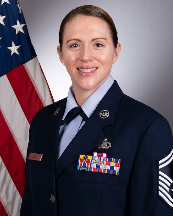 Official Photo of SMSgt Chantelle Friedman, wearing blue service dress in front of an American flag.