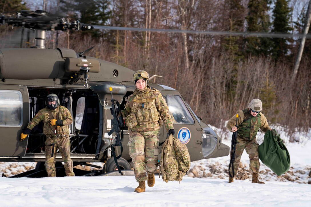 Three airmen walk from a parked helicopter in the snow.