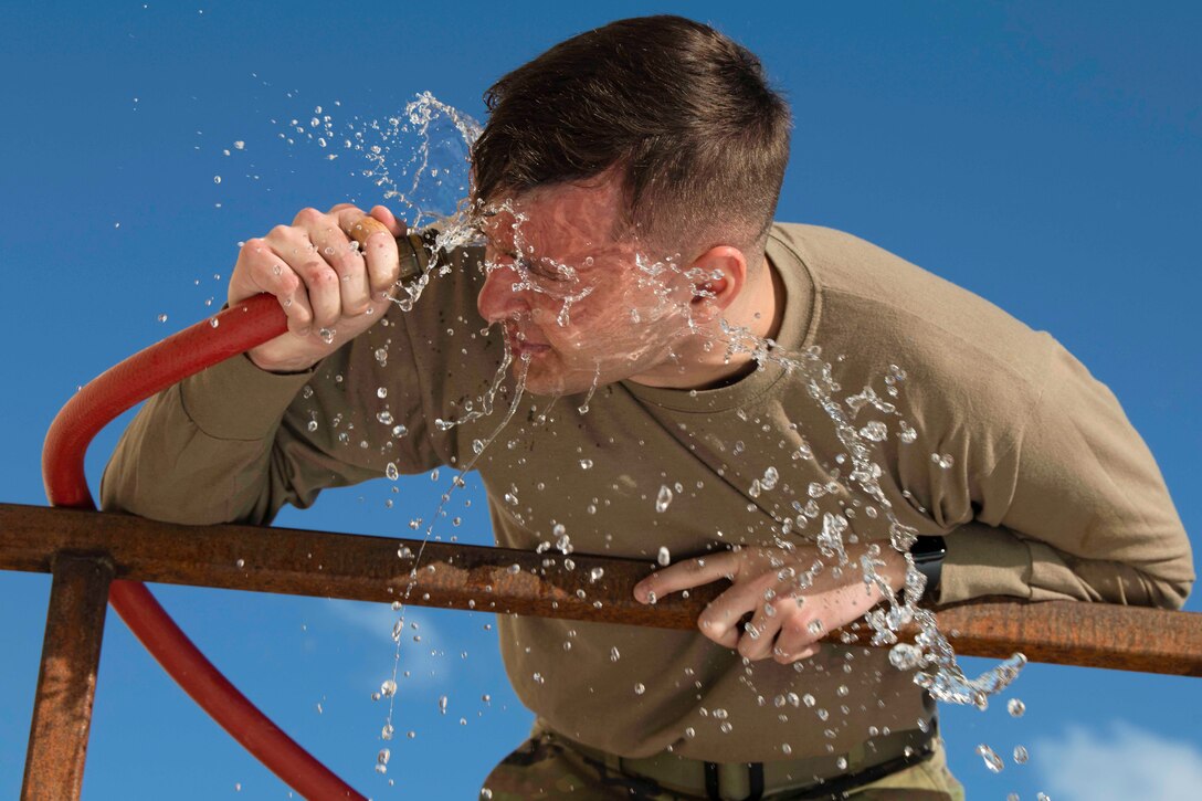 An airman uses a water hose to wash his face.