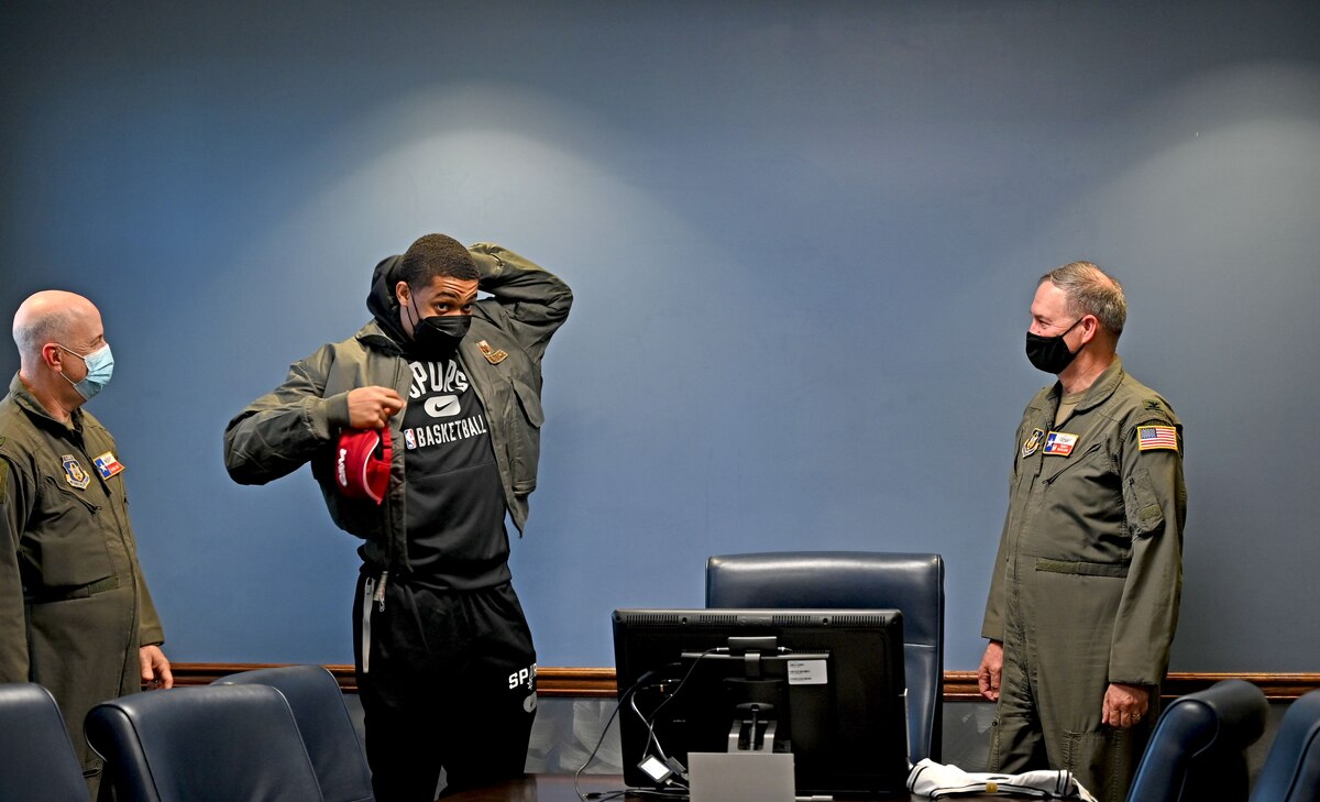 Keldon Johnson, a San Antonio Spurs basketball player, dons an Air Force flight jacket during a visit to the 433rd Airlift Wing at Joint Base San Antonio-Lackland, Texas, March 2, 2022. Col. Terry McClain, 433rd AW commander (right), and Col. James Miller, 433rd Operations Group commander (left), gave Johnson the jacket to welcome him to the wing. (U.S. Air Force photo by Samantha Mathison)