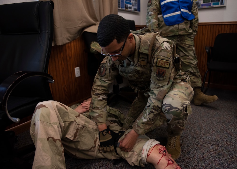 An Airman applies a tourniquet around a leg of a simulated, injured Airman.