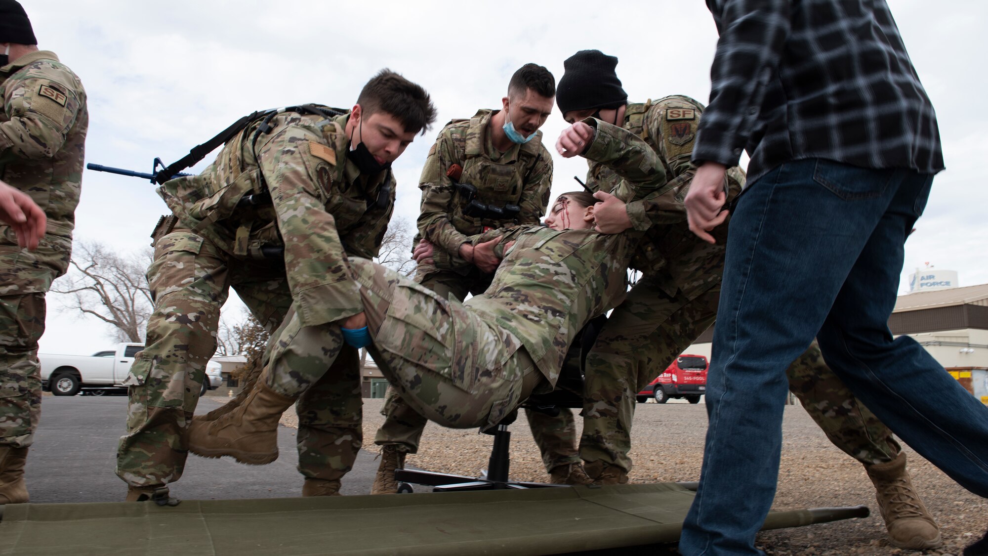 A group of Airmen lowers a simulated, injured Airman to a stretcher.
