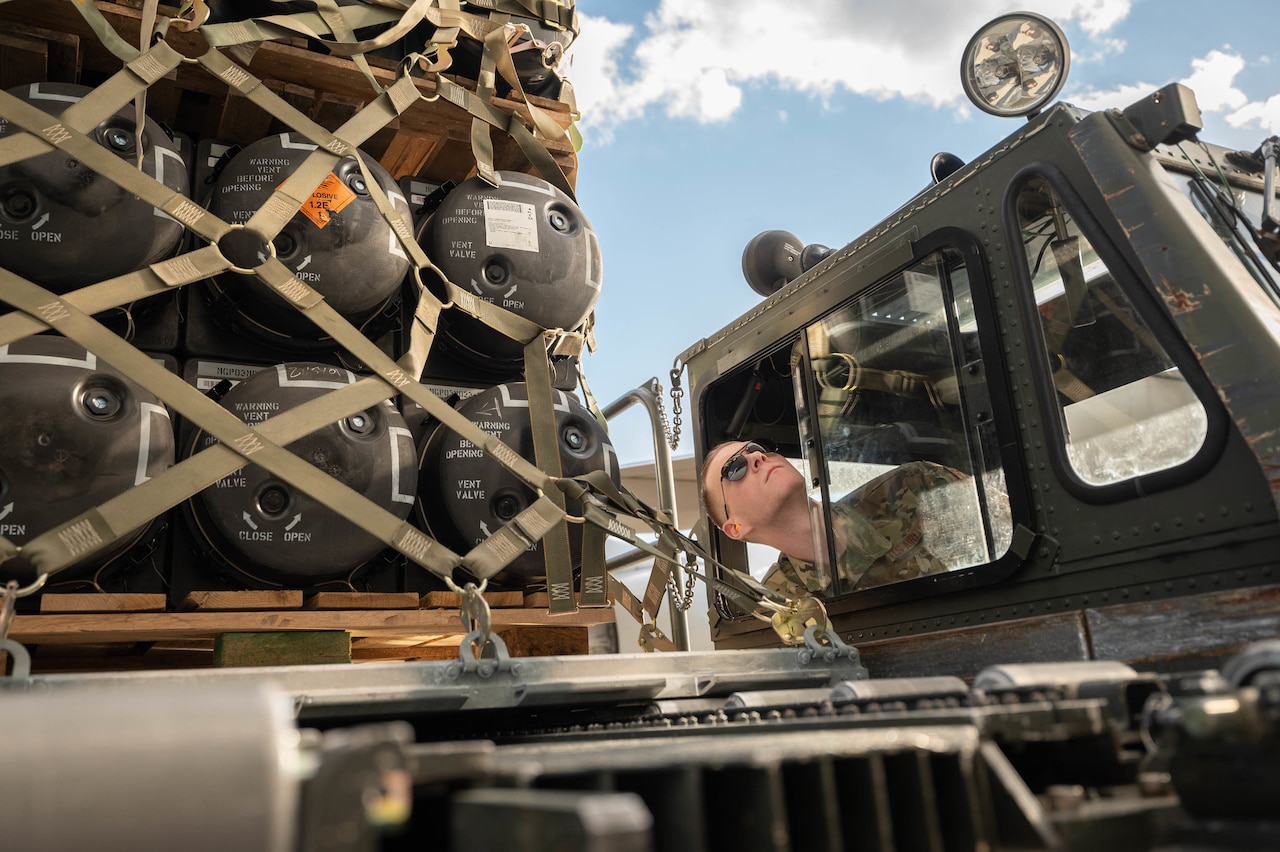 A service member pokes his head out of the window of a vehicle.