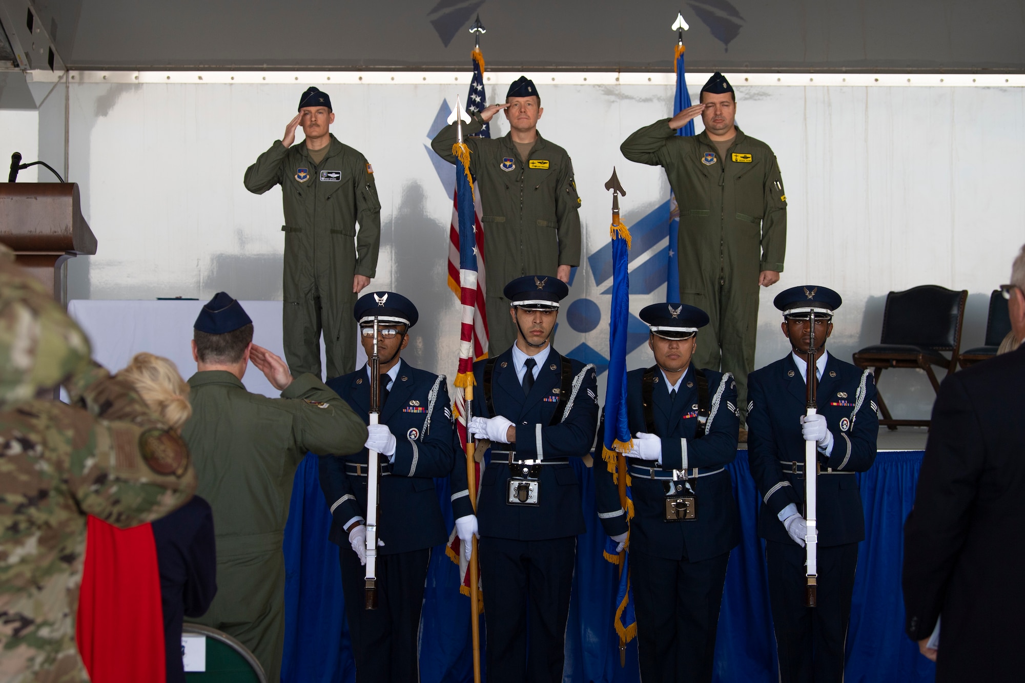 A photo of honor guard members presenting the colors and three service members saluting behind them on stage.