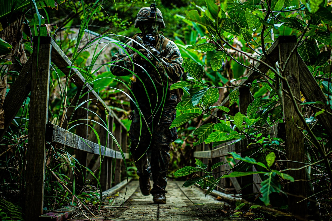 A U.S. Marine with 3d Marine Division assaults an objective during the squad attack phase of the 3d Marine Division Squad Competition at the Jungle Warfare Training Center on Camp Gonsalves, Okinawa, Japan, Jan. 6, 2022. The week-long competition tests jungle survival skills, basic infantry tactics, and excellence in weapons handling. The competition participants are forward-deployed in the Indo-Pacific under 4th Marines, 3d Marine Division, as a part of the Unit Deployment Program. (U.S. Marine Corps photo illustration by Lance Cpl. Jonathan Willcox)
