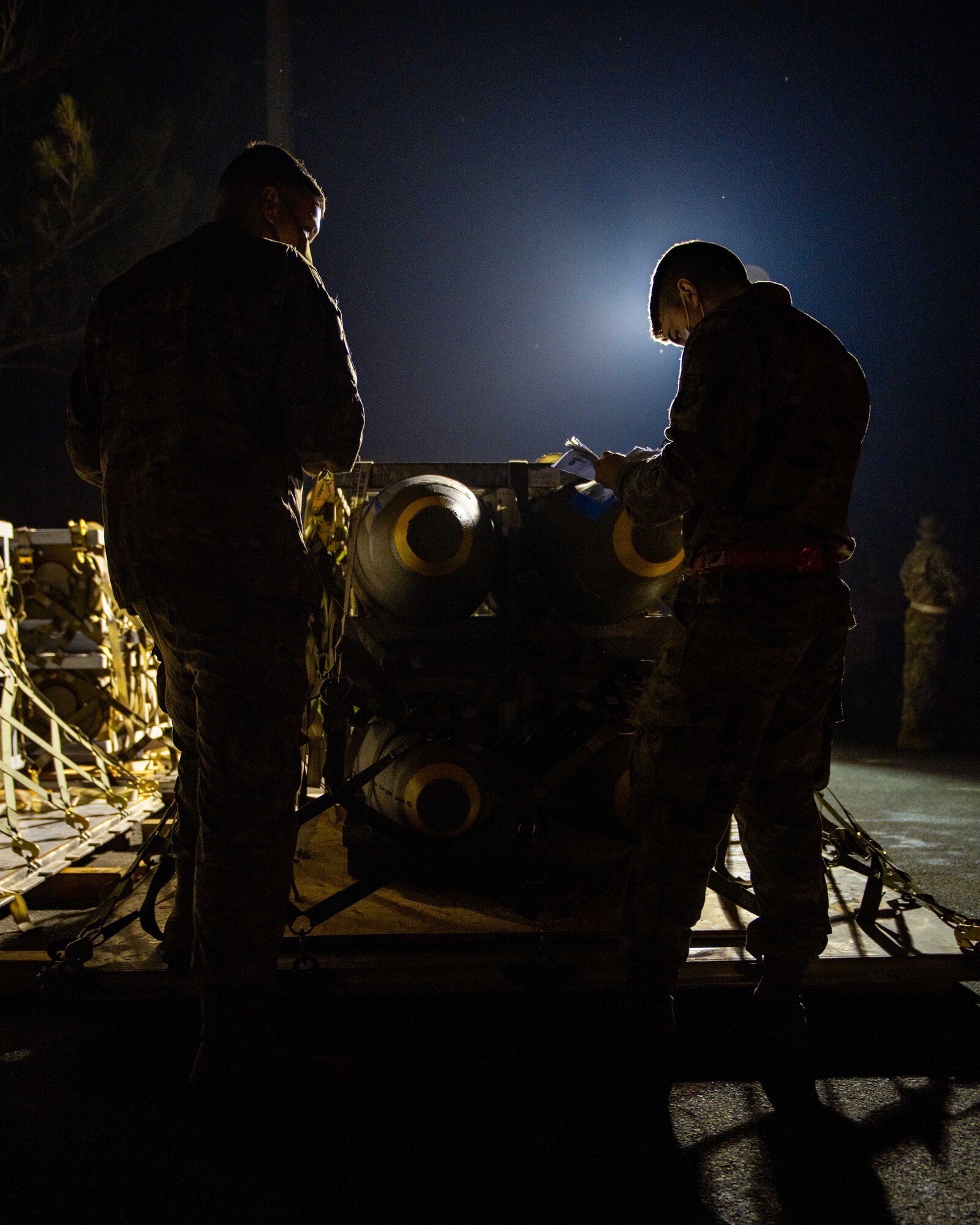Two Airmen inspect a pallet of munitions at night